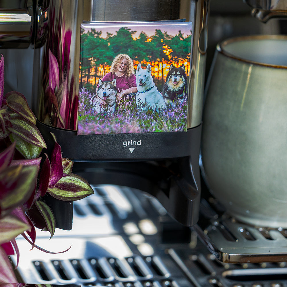 Quadratischer Fotomagnet mit einer Person und drei Hunden, angebracht an einer Kaffeemaschine