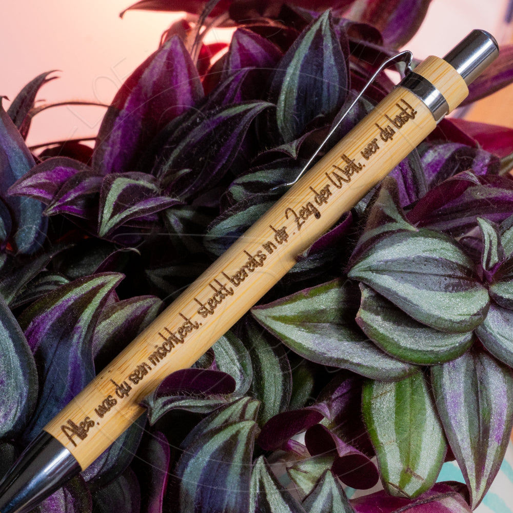 Bambus-Kugelschreiber mit eingraviertem Sinnspruch, arrangiert auf dunkelvioletten Pflanzenblättern