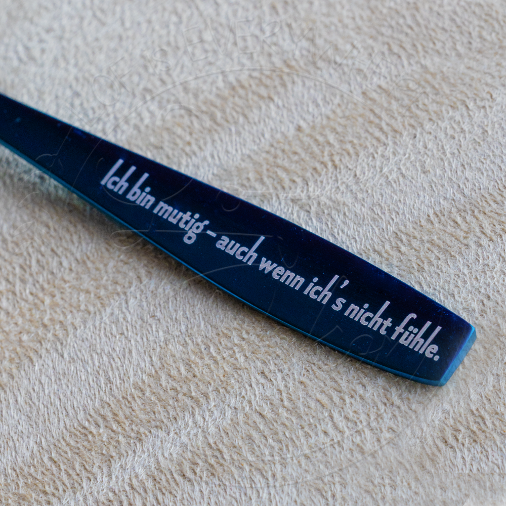 Detailaufnahme eines dunklen Kinderlöffels mit Gravur ‚Ich bin mutig – auch wenn ich’s nicht fühle